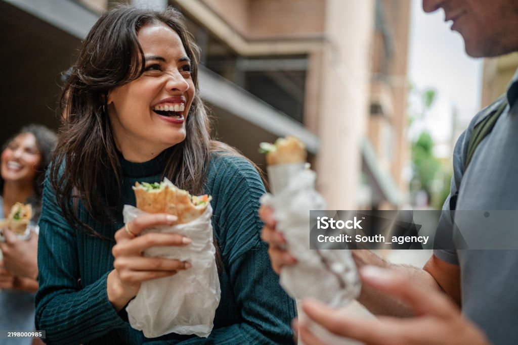 A group of young adults in Sydney share smiles and laughter as they enjoy delicious street food together. The lively atmosphere captures the joy of weekend leisure activities in the city.